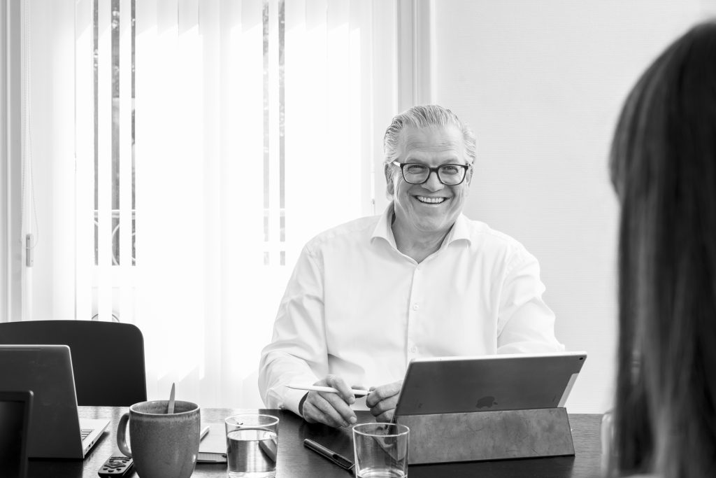 Dirk Spiegel im Gespräch bei Velaw, am Tisch mit Laptop und Unterlagen